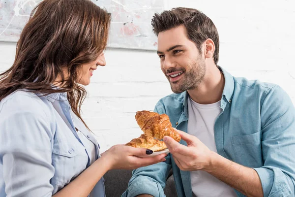 Schönes Paar, das sich beim Frühstück zu Hause anschaut und Croissants isst — Stockfoto