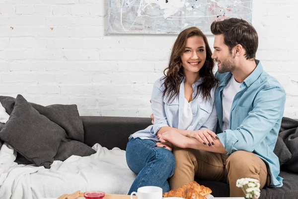 Усміхнена пара сидить на дивані і тримає руки у вітальні — Stock Photo