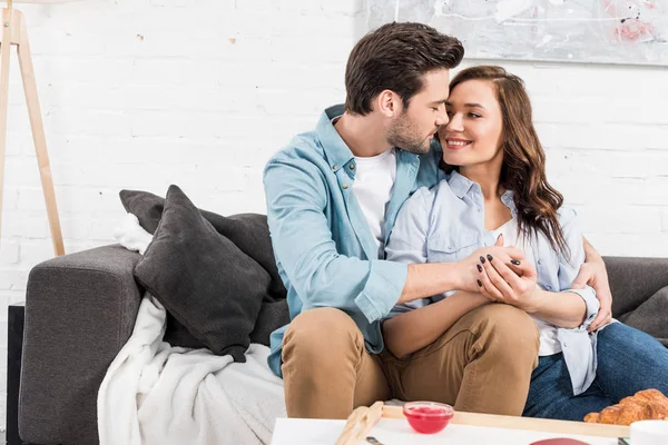 Happy couple sitting on couch and holding hands in living room — Stock Photo