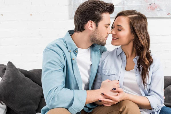 Schönes Paar sitzt auf der Couch und hält die Hände zu Hause, während die Frau in die Kamera schaut — Stockfoto