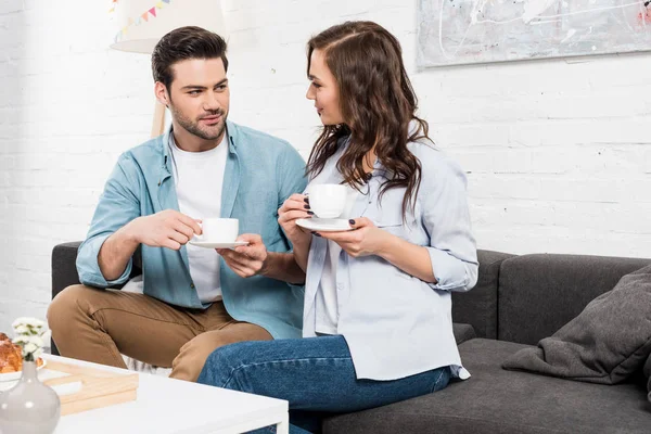 Beautiful couple sitting on couch and drinking coffee during breakfast at home — Stock Photo