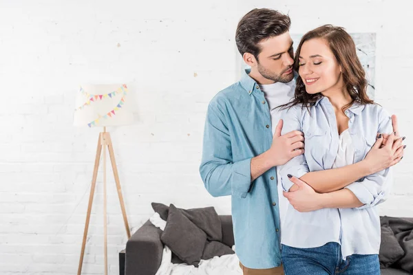 Handsome man embracing happy woman at home — Stock Photo
