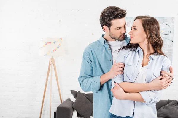 Hombre tiernamente abrazando atractiva mujer en casa - foto de stock