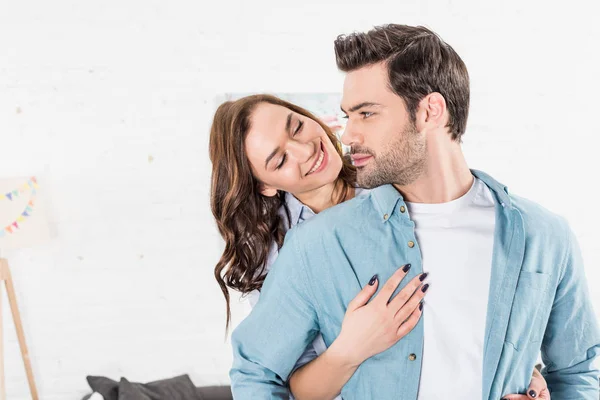 Mujer sonriente abrazando al hombre desde atrás en casa - foto de stock