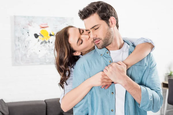 Mujer abrazando y besando hombre desde atrás en casa - foto de stock