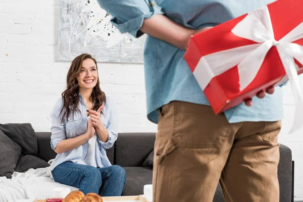 Vue arrière de l'homme tenant cadeau d'anniversaire rouge derrière le dos avec femme excitée sur fond — Photo de stock