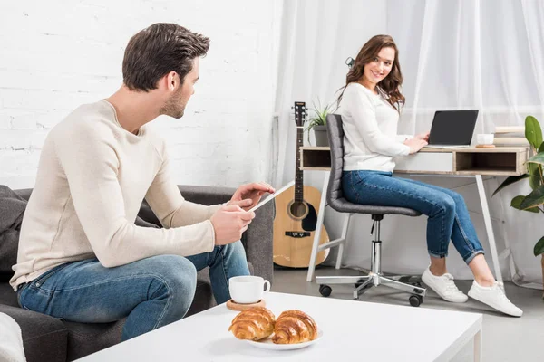 Mann nutzt digitales Tablet, während Frau am Computer-Schreibtisch im Wohnzimmer sitzt — Stockfoto