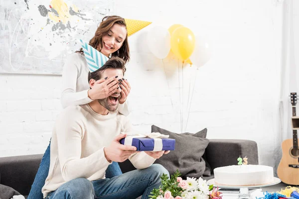 Mulher surpreendente animado homem com presente de aniversário na sala de estar — Fotografia de Stock