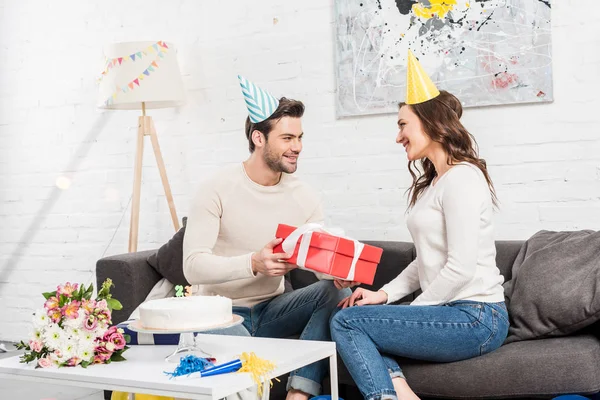 Feliz casal celebrando aniversário e homem apresentando caixa de presente para a mulher na sala de estar — Stock Photo