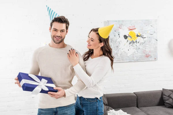 Schönes glückliches Paar mit Geschenkbox umarmt und feiert Geburtstag im Wohnzimmer — Stockfoto