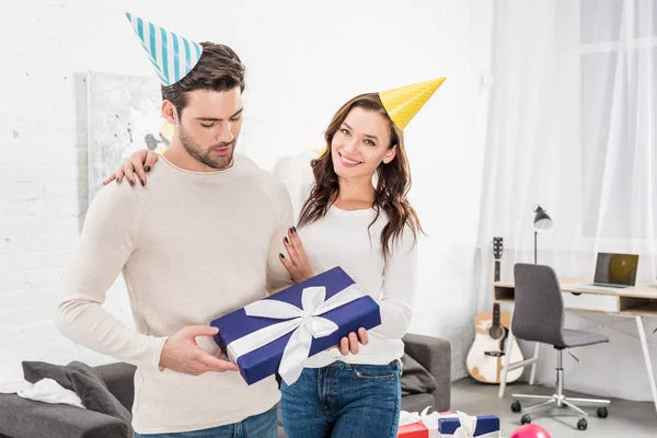 Belo casal com caixa de presente abraçando e celebrando aniversário na sala de estar — Fotografia de Stock