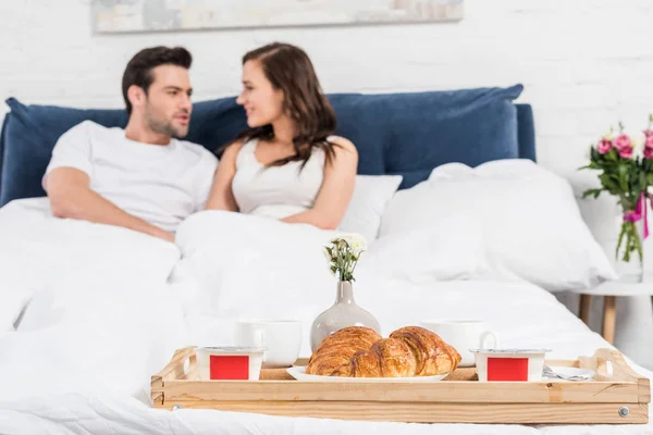 Focalizzazione selettiva del cibo per la colazione su vassoio con coppia sdraiata a letto sullo sfondo — Foto stock