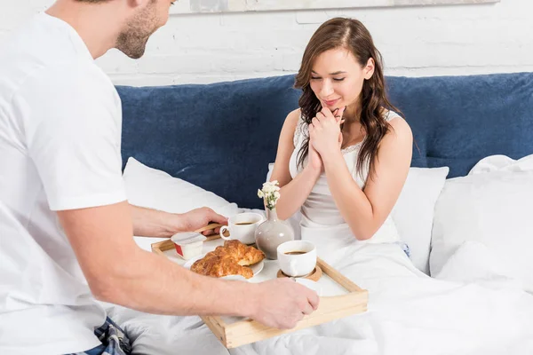 Hombre sorprendente mujer con desayuno en la cama en casa por la mañana - foto de stock