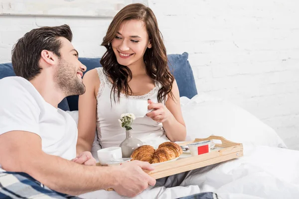 Smiling couple lying in bed and having breakfast in morning — Stock Photo