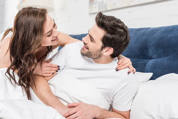 Hermosa pareja feliz abrazándose y mirándose en la cama - foto de stock