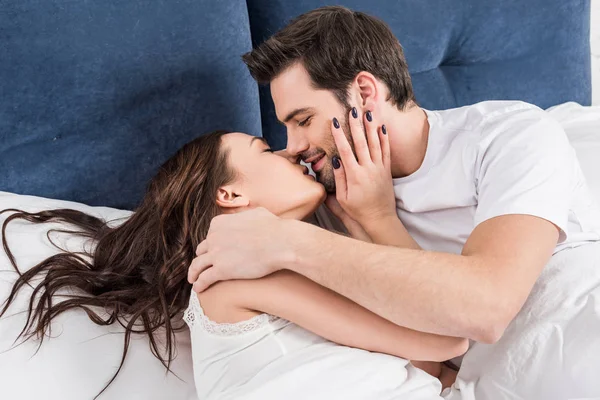 Belo casal em roupa de noite beijando na cama em casa — Fotografia de Stock