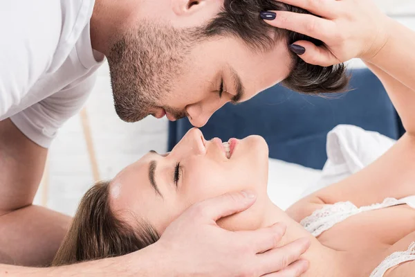 Close up de casal com os olhos fechados tocando uns aos outros na cama — Fotografia de Stock