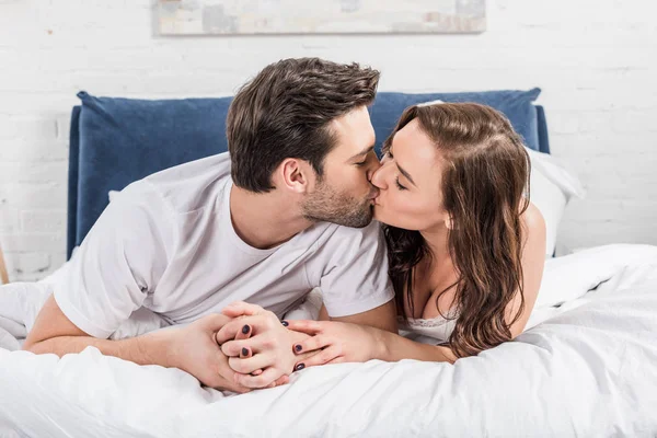 Belo casal em roupa de noite beijando na cama em casa — Fotografia de Stock