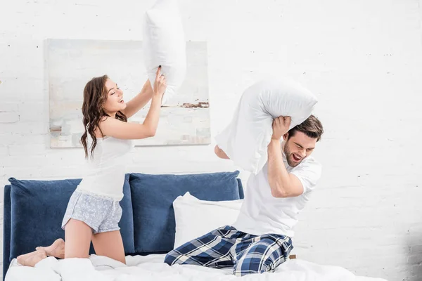 Casal em pijama lutando com travesseiros no quarto — Fotografia de Stock
