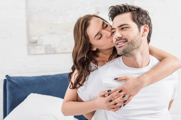 Mujer tiernamente abrazar y besar hombre guapo en la cama - foto de stock