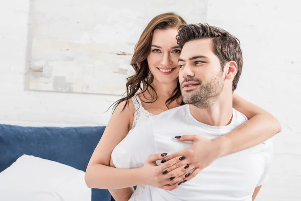 Frau umarmt Mann zärtlich und blickt im Bett in Kamera — Stockfoto