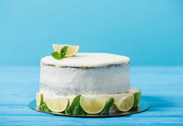 Gâteau blanc décoré avec des tranches de citron vert sur la table isolée sur bleu — Photo de stock