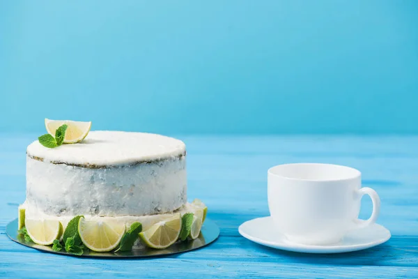 Pastel decorado con rodajas de lima cerca de la taza de té aislado en azul - foto de stock