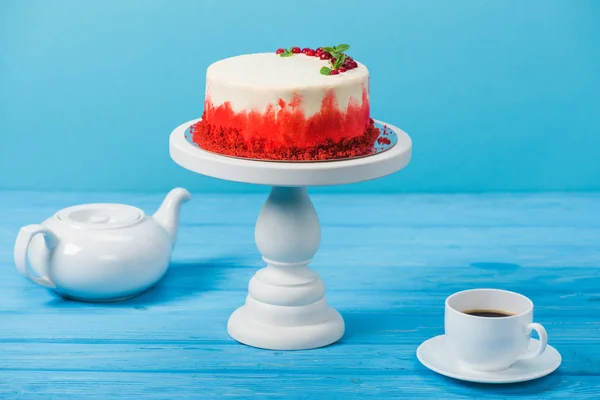 Pastel decorado con grosellas rojas y hojas de menta, taza blanca y tetera aislada en azul - foto de stock