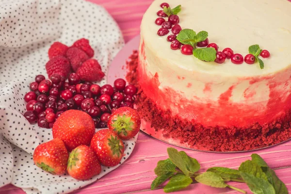 Close up of white cake decorated with currants and mint leaves near fruits on pink surface — Stock Photo