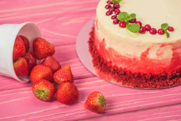 Close up of white cake decorated with currants and mint leaves near fruits on pink wooden surface — Stock Photo