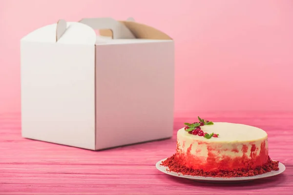 Pastel decorado con grosellas y hojas de menta cerca de paquete blanco aislado en rosa - foto de stock