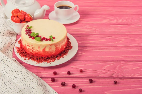 Close up of cake decorated with currants and mint leaves near tea pot and cup of strawberries on pink surface — Stock Photo