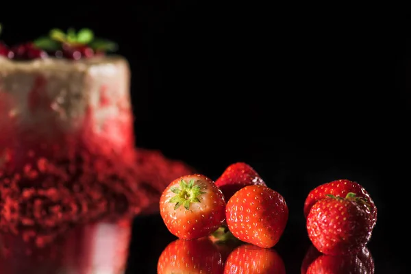 Selective focus of white cake decorated with red currants and mint leaves near strawberries isolated on black — Stock Photo