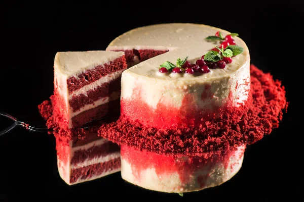 Gâteau blanc décoré de feuilles de menthe et de groseilles rouges près de la spatule avec morceau de gâteau isolé sur noir — Photo de stock