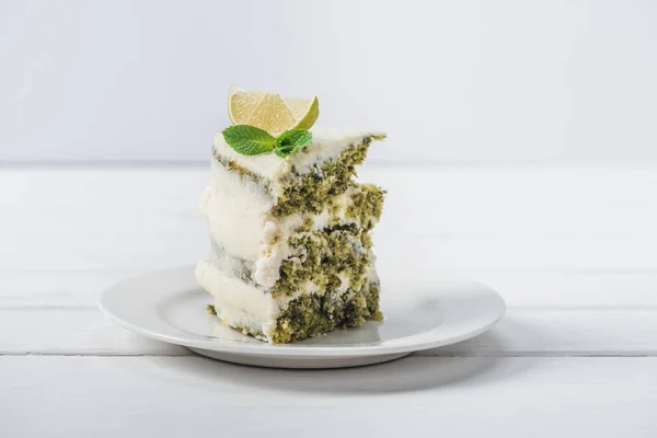 Pezzo di torta bianca decorata con foglie di menta e fette di linea isolate su bianco — Foto stock