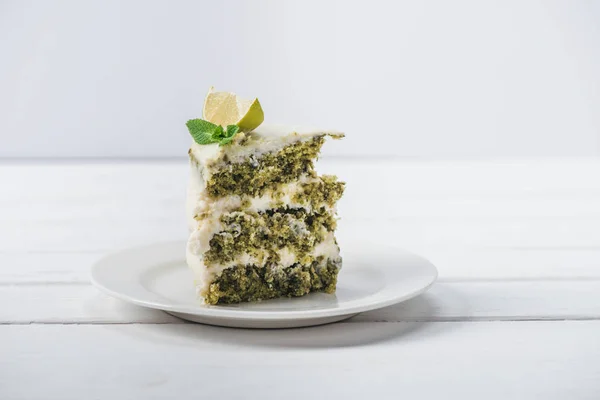 Pezzo di torta bianca decorata con foglie di menta e fette di linea su piattino isolato su bianco — Foto stock