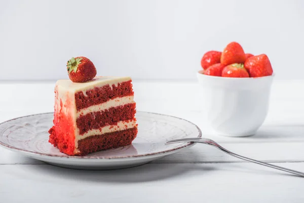 Piece of red cake decorated with strawberry on saucer near cup of fruits isolated on white — Stock Photo