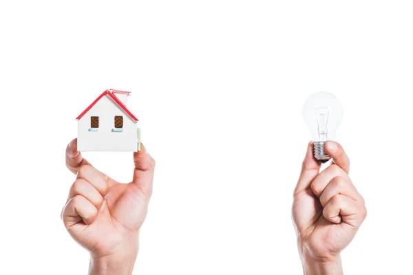 Vista recortada de manos masculinas sosteniendo modelo de casa y lámpara led en manos aisladas en blanco, concepto de eficiencia energética en el hogar - foto de stock