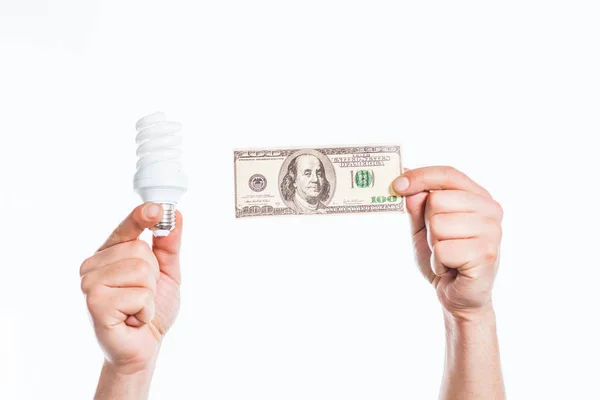 Обрезанный вид мужских рук, держащих флуоресцентную лампу и банкноту 100 долларов в руках, изолированных на белом, концепция энергоэффективности — стоковое фото