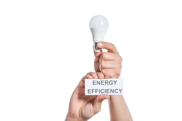 Cropped view of man holding fluorescent lamp and paper card with lettering isolated on white, energy efficiency concept — Stock Photo