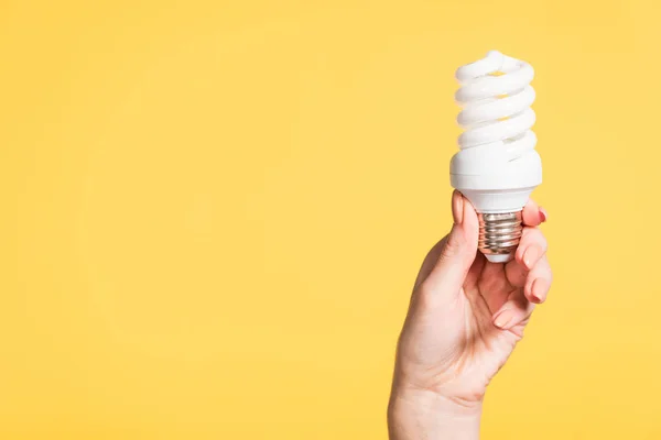 Vista cortada da mão fêmea segurando lâmpada fluorescente isolada no amarelo, conceito de eficiência energética — Fotografia de Stock