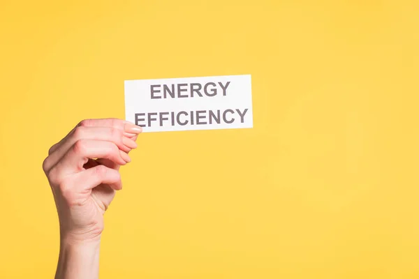 Vista recortada de la tarjeta de papel de mano femenina con letras aisladas en amarillo, concepto de eficiencia energética - foto de stock