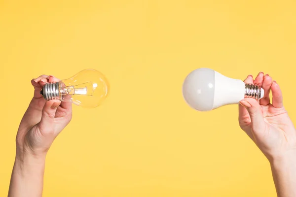 Vista recortada de las manos femeninas sosteniendo la lámpara led y fluorescente aislada en amarillo, concepto de eficiencia energética - foto de stock