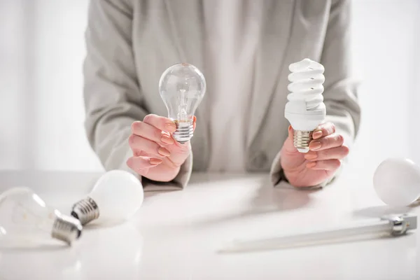 Visão cortada da mulher segurando lâmpadas led e fluorescentes no fundo branco, conceito de eficiência energética — Fotografia de Stock