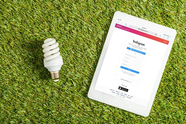 Вид зверху Лампа люмінесцентна поблизу Цифрова табличка з instagram app на екрані по зеленій траві, енергетичної ефективності концепції — стокове фото