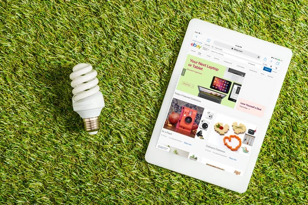 Vista dall'alto della lampada fluorescente vicino al tablet digitale con app ebay sullo schermo su erba verde, concetto di efficienza energetica — Foto stock