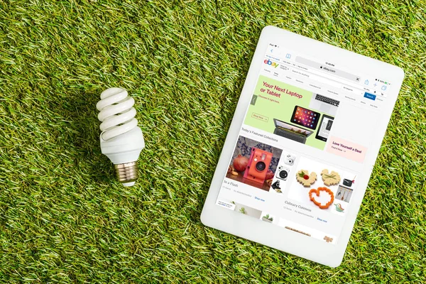 Ansicht der Leuchtstofflampe in der Nähe digitales Tablet mit ebay App auf dem Bildschirm auf grünem Gras, Energieeffizienzkonzept — Stock Photo