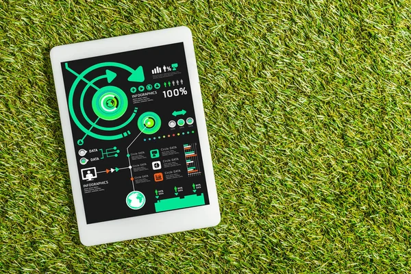 Vista superior de la tableta digital con gráficos en pantalla sobre césped verde, concepto de eficiencia energética - foto de stock