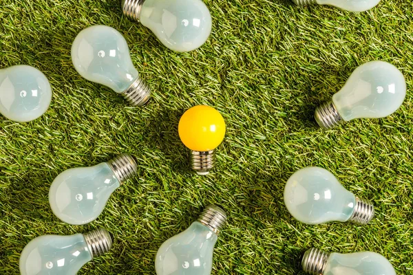 Vista superior de lâmpadas fluorescentes perto de lâmpada amarela na grama verde, conceito de eficiência energética — Fotografia de Stock