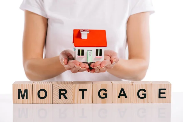 Cropped view of woman holding house model near wooden cubes with mortgage lettering isolated on white — Stock Photo